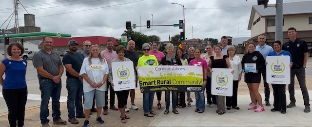 Community members and local leaders gather in downtown Brookfield to celebrate Brookfield’s designation as a Smart Rural Community, holding recognition signs and a congratulatory banner.